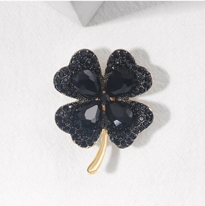 Macro detail of a golden four-leaf clover brooch featuring black crystals and pavé setting