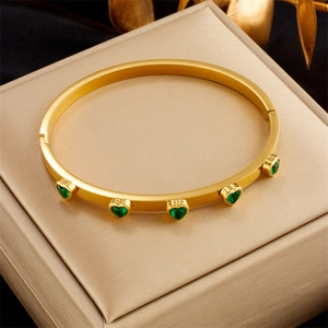 Gold plated stainless steel bangle with five emerald green heart stones on a gold box