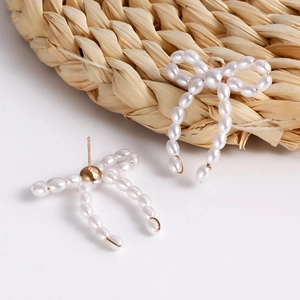 Macro shot of handmade pearl bow earrings with golden studs on a woven texture
