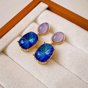 Close-up of vintage gold earrings with purple and blue crystals on beige velvet padding