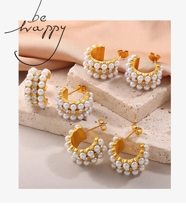 Close-up of gold-plated C-shaped earrings with pearls and crystals on beige stone