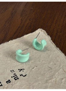 Detail of mint green C-shaped resin earrings with glossy finish on textured paper