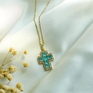 Detailed view of a gold cross necklace with turquoise zircons on white silk background