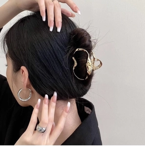 Close-up of a hollow liquid gold metal hair claw clip holding a stylish low bun hairstyle