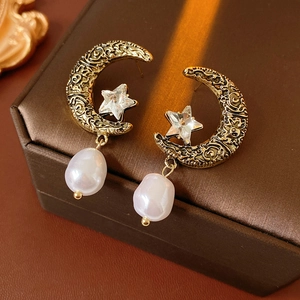 Detailed close-up of vintage gold moon and star earrings with diamonds and white pearls