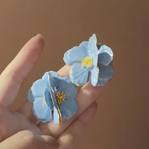Macro detail of blue floral earrings with golden stamens and glossy petal finish