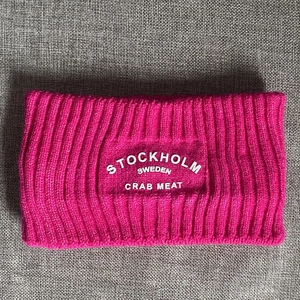 Detail des rosa-violetten Strickstirnbandes mit weißer Stockholm Sweden Bestickung