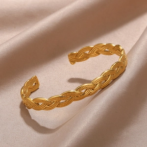 Macro shot of gold woven cuff bracelet showing detailed braided texture on beige silk
