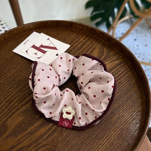 Detailed shot of pink polka dot scrunchie with AE ALLINE brand tag on wooden tray