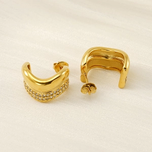 Macro detail of gold U-shaped earrings with micro-pave cubic zirconia on beige fabric
