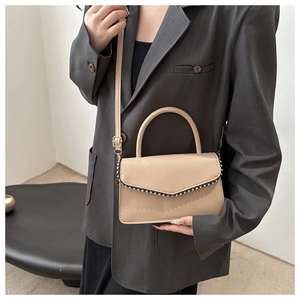 Detail of khaki crossbody bag with rivet edges worn with a dark grey blazer