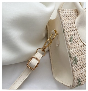 Close-up of golden hardware hooks and adjustable strap on a woven straw handbag