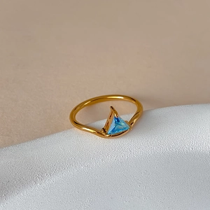 Detailed view of wave-shaped 18k gold ring with a triangular light blue zircon stone