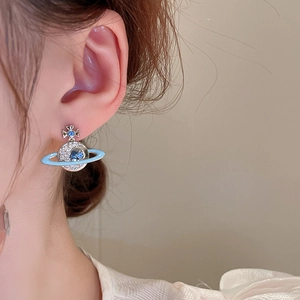 Close-up of light blue enamel planet earrings with crystals on a model's ear