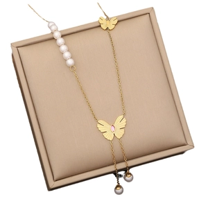 Élégant collier papillon doré avec perles et pierre rose dans un écrin de bijoux beige