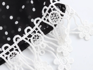 Detail of elegant white floral lace trim on a black polka dot dress fabric closeup