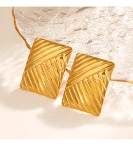 Detail view of textured gold rectangular earrings on a glass plate with natural lighting