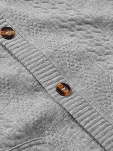 Detail of grey knitted cardigan with jacquard diamond pattern and brown textured buttons