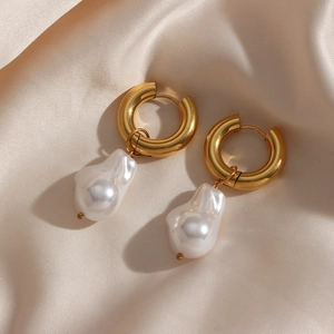 Close-up of Baroque pearl pendant earrings with golden hoops on beige silk fabric