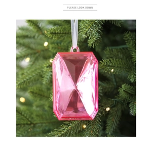Close-up of a pink faceted acrylic gemstone ornament with a white ribbon on a festive tree