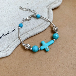 Close-up of beaded turquoise bracelet featuring a silver cross pendant and lobster clasp