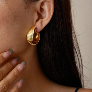 Close-up of golden multi-layer textured clip-on earring on model with metallic finish