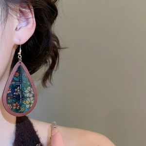 Detail of teardrop wooden earring with colorful floral pattern on a female model