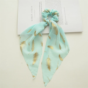 Detail of mint green chiffon scrunchie with golden feather patterns on a magazine