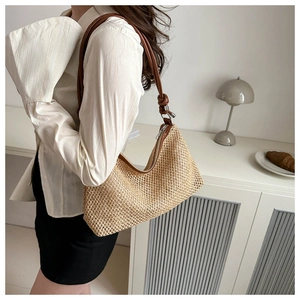 Detail of hand-woven straw shoulder bag with brown leather strap and knotted accents