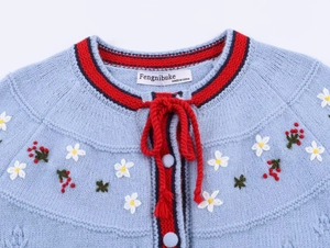 Close-up of blue knit cardigan with red drawstring bow and floral embroidery details