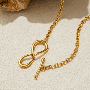 Détail du pendentif nœud en acier doré avec fermoir OT sur surface texturée