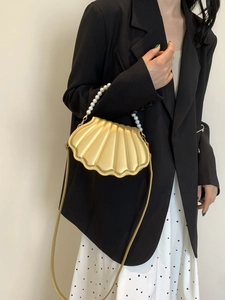 Detail of a golden shell-shaped handbag featuring textured ribs and pearl bead handle
