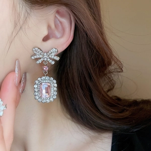 Détail de boucles d'oreilles nœud argenté avec un pendentif carré en zircon rose