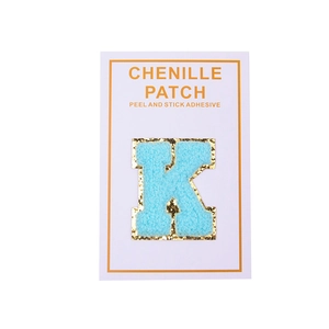 Close-up of light blue chenille letter K patch with gold glitter edge and adhesive back