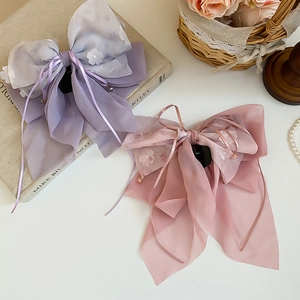 Dettaglio di grandi fermagli per capelli a fiocco in chiffon con motivi floreali bianchi