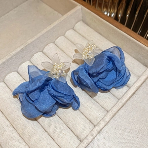 Détail de boucles d'oreilles rose en tissu bleu avec étamines en perles en boîte