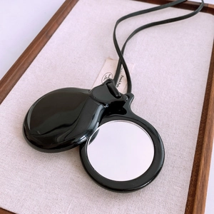 Detail of a portable round black leather mirror necklace on a rustic wooden tray
