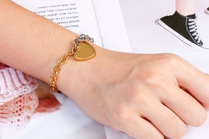 Macro shot of two-tone gold and silver chain bracelet featuring a polished heart pendant