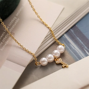 Close-up of golden necklace with white pearls and a crystal-set key pendant charm
