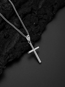 Pendentif croix argenté avec fine chaîne maille gourmette sur fond de charbon de bois