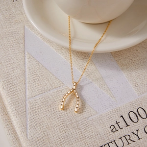 Détail d'un collier pendentif wishbone doré serti de zircons cubiques de taille baguette