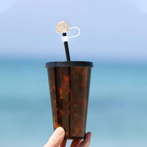 Close-up of a white flower straw topper on a tortoise shell tumbler at the beach