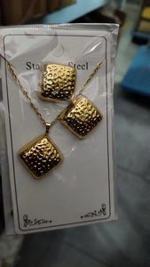 Detailed close-up of golden stainless steel square pendant jewelry set with leaf texture