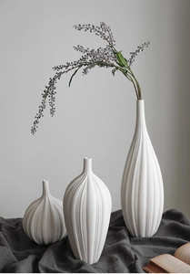 Primo piano di tre vasi in ceramica opaca bianca con scanalature verticali su tessuto grigio