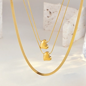 Macro shot of layered gold herringbone chain and 3D heart pendants on white stone