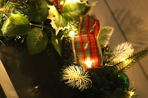 Detail of Christmas wreath with red plaid ribbons and warm LED lights on a wooden door