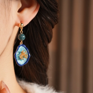Close-up of vintage flower earrings with blue enamel and gold details on a model