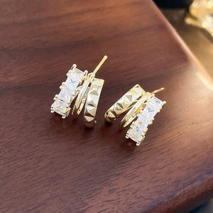 Macro detail of gold-plated multi-layer C-shape earrings with cubic zirconia and studs