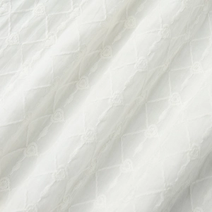 Détail macro du tissu brodé blanc avec motifs de losanges et petits cœurs ajourés