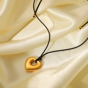 Close-up of golden hollow heart pendant on black cord over cream silk fabric